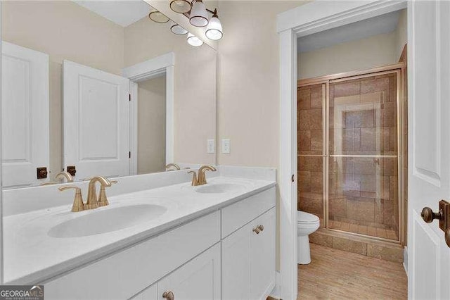 bathroom with a stall shower, toilet, double vanity, and a sink