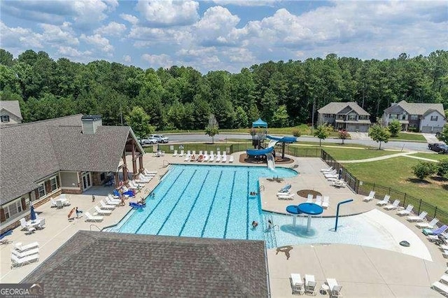 pool featuring a water slide, fence, a view of trees, and a patio area