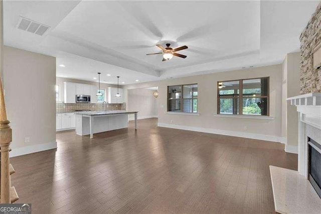 unfurnished living room featuring dark wood-style floors, a fireplace, a tray ceiling, a ceiling fan, and visible vents