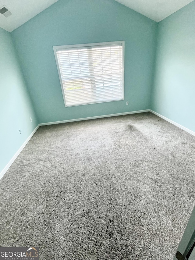 carpeted spare room featuring visible vents, baseboards, and lofted ceiling