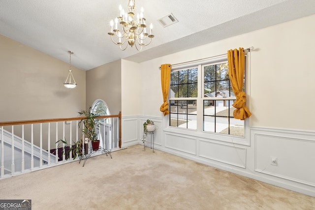 carpeted spare room with a textured ceiling, lofted ceiling, and a notable chandelier