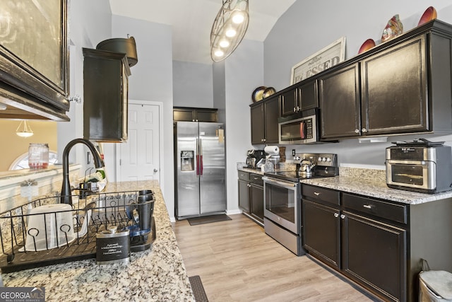 kitchen with light wood-type flooring, stainless steel appliances, hanging light fixtures, light stone countertops, and dark brown cabinets