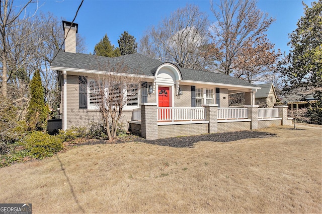 view of front of home with brick siding, roof with shingles, a chimney, covered porch, and a front yard