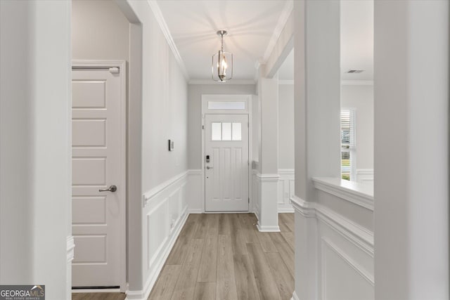 doorway to outside with a notable chandelier, light hardwood / wood-style floors, crown molding, and a wealth of natural light