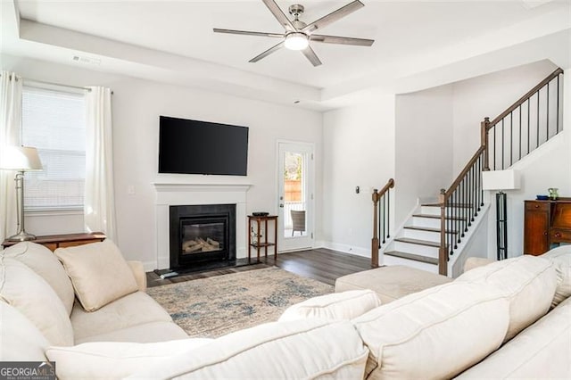 living room with a tray ceiling, dark wood-type flooring, and ceiling fan