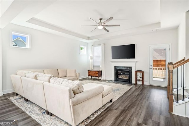 living room featuring ceiling fan, plenty of natural light, a tray ceiling, and dark wood-type flooring