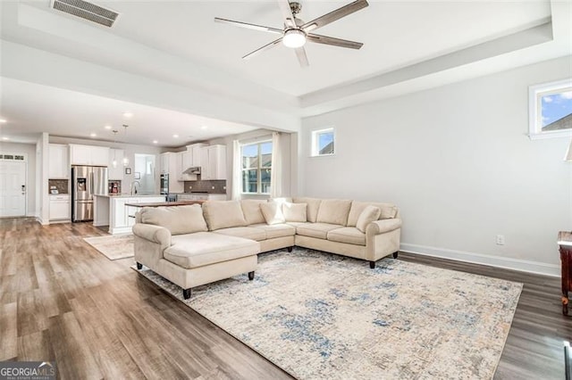 living room with a tray ceiling, hardwood / wood-style flooring, and ceiling fan