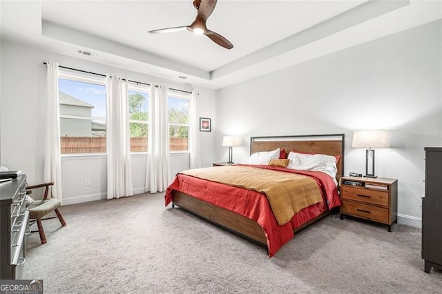 carpeted bedroom featuring a raised ceiling and ceiling fan