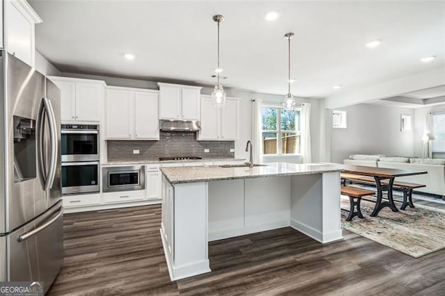 kitchen featuring sink, white cabinetry, decorative light fixtures, stainless steel appliances, and an island with sink