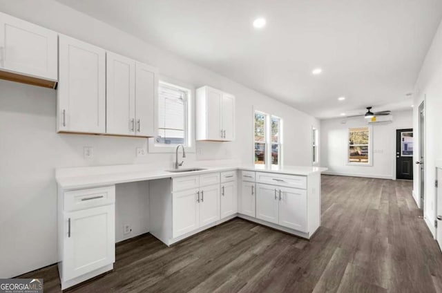 kitchen with dark wood-type flooring, sink, kitchen peninsula, and white cabinets