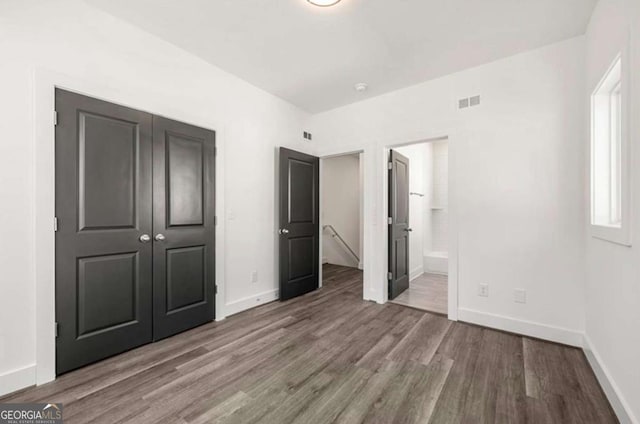 unfurnished bedroom with a closet, ensuite bathroom, and hardwood / wood-style floors