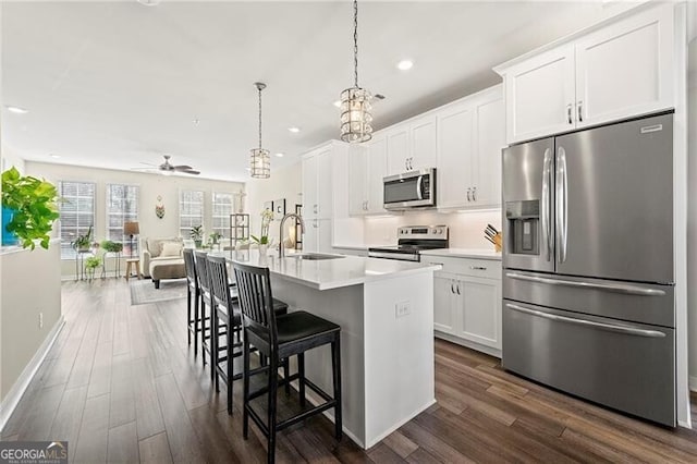 kitchen featuring a center island with sink, stainless steel appliances, hanging light fixtures, sink, and white cabinets