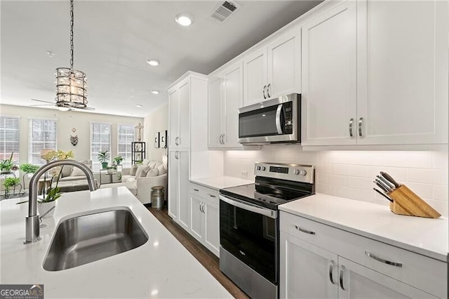 kitchen featuring sink, appliances with stainless steel finishes, white cabinets, decorative backsplash, and pendant lighting