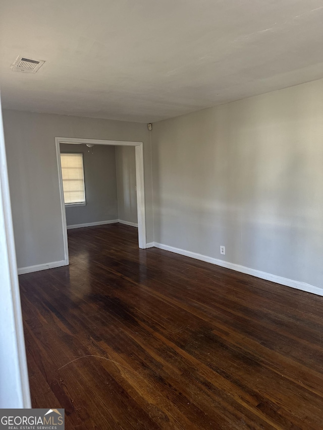 spare room with baseboards, visible vents, and dark wood-style flooring