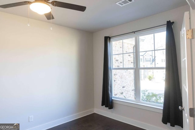 empty room with baseboards, visible vents, ceiling fan, and dark wood-type flooring