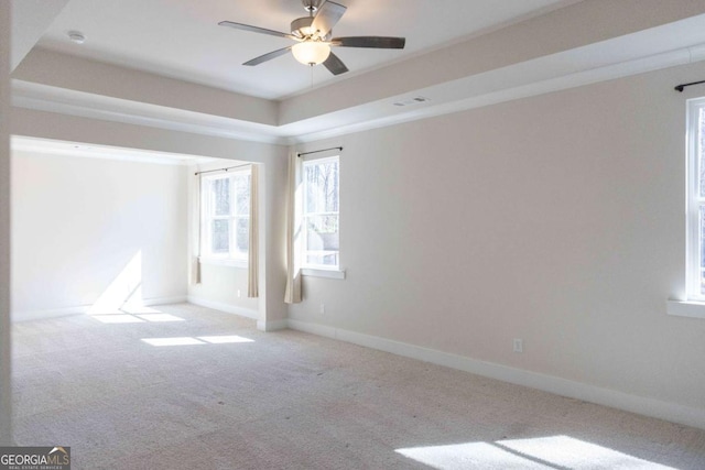 carpeted spare room with a raised ceiling, visible vents, ceiling fan, and baseboards