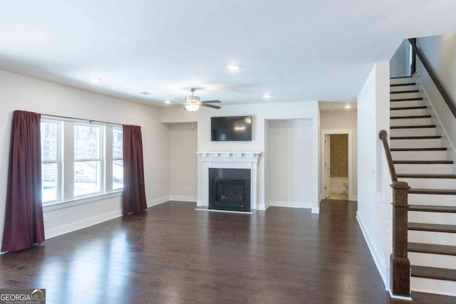 unfurnished living room featuring dark wood finished floors, baseboards, a ceiling fan, and stairs