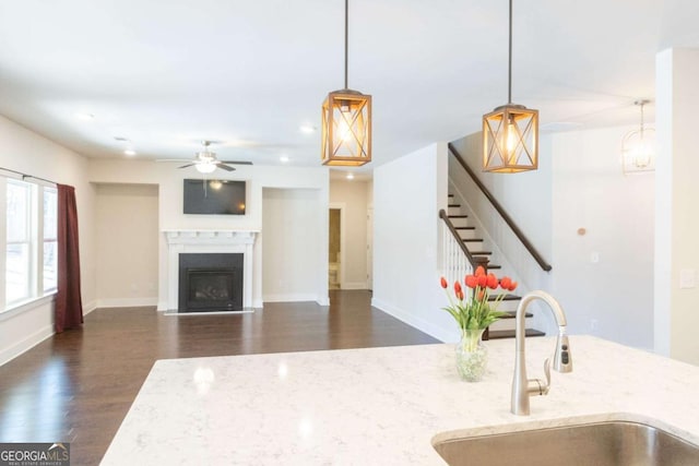 kitchen with light stone counters, a fireplace with flush hearth, a sink, wood finished floors, and a ceiling fan