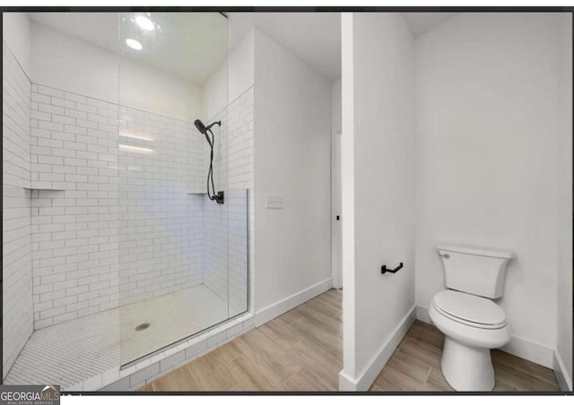 bathroom featuring tiled shower, wood-type flooring, and toilet