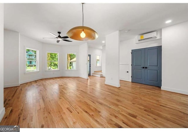 unfurnished living room featuring an AC wall unit, ceiling fan, and wood-type flooring