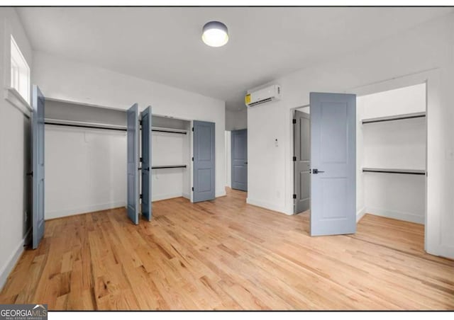 unfurnished bedroom with multiple closets, light hardwood / wood-style floors, and a wall mounted air conditioner