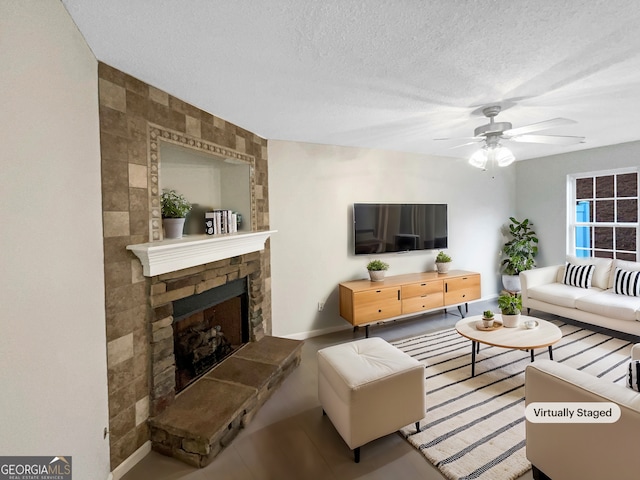 living room with ceiling fan, a stone fireplace, and a textured ceiling