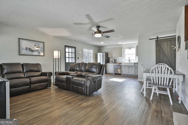 living room with a textured ceiling, ceiling fan, dark hardwood / wood-style flooring, a barn door, and sink