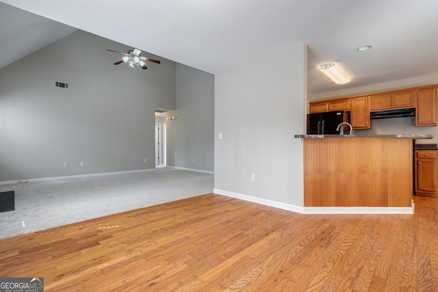 kitchen featuring brown cabinetry, freestanding refrigerator, open floor plan, under cabinet range hood, and baseboards