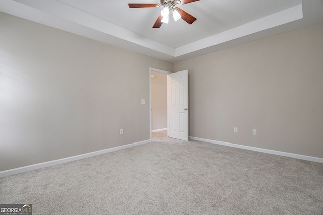 unfurnished room with light carpet, ceiling fan, baseboards, and a raised ceiling