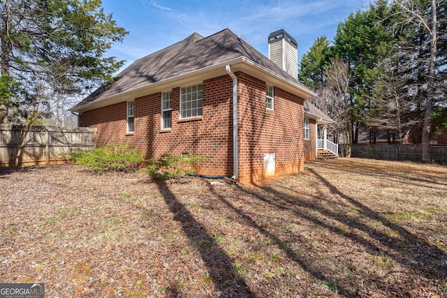 view of side of home with crawl space, brick siding, fence, and a chimney