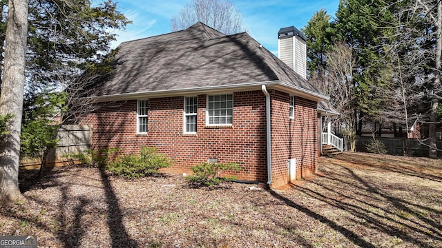 view of side of property with brick siding, fence, a chimney, and roof with shingles