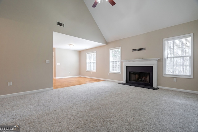 unfurnished living room featuring visible vents, a fireplace with flush hearth, light carpet, high vaulted ceiling, and baseboards