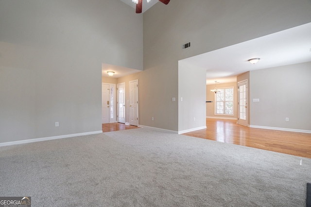 unfurnished living room featuring light carpet, baseboards, visible vents, and ceiling fan with notable chandelier