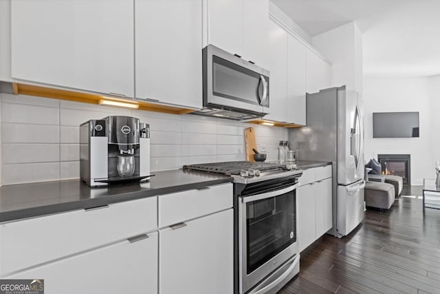 kitchen with white cabinets, a glass covered fireplace, dark countertops, dark wood-style floors, and appliances with stainless steel finishes