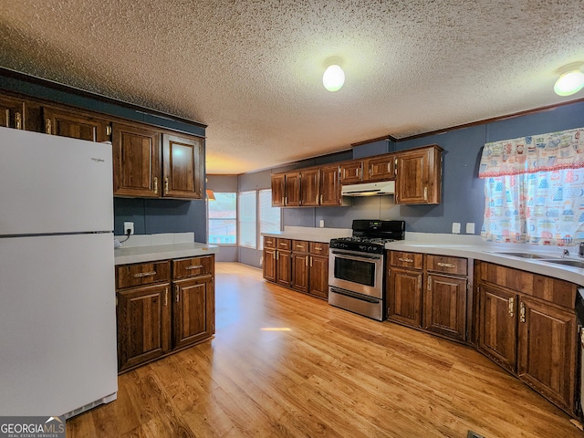 kitchen with light hardwood / wood-style flooring, stainless steel gas stove, a textured ceiling, white fridge, and sink