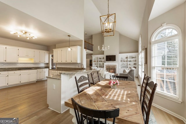 dining space featuring a chandelier, high vaulted ceiling, a warm lit fireplace, and light wood-type flooring