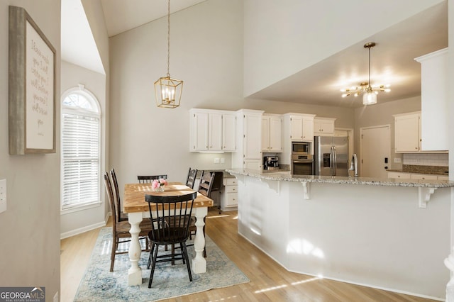 dining area with an inviting chandelier, light wood-style flooring, high vaulted ceiling, and baseboards