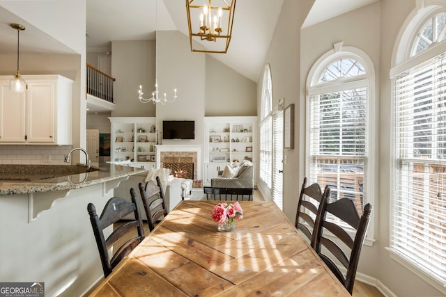 dining area featuring a chandelier, high vaulted ceiling, and a premium fireplace