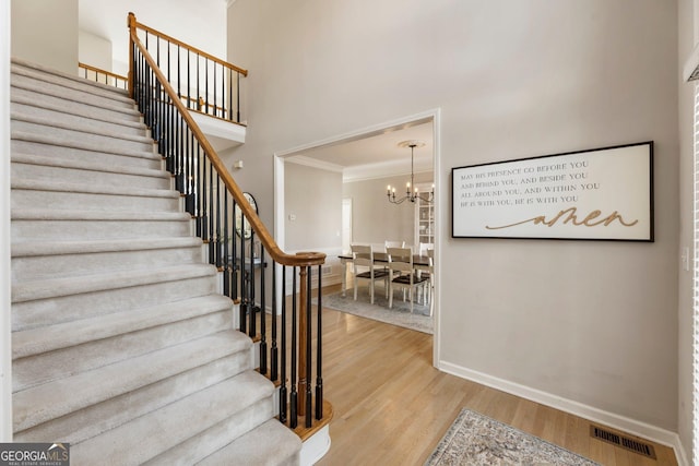 staircase featuring baseboards, visible vents, ornamental molding, wood finished floors, and a high ceiling