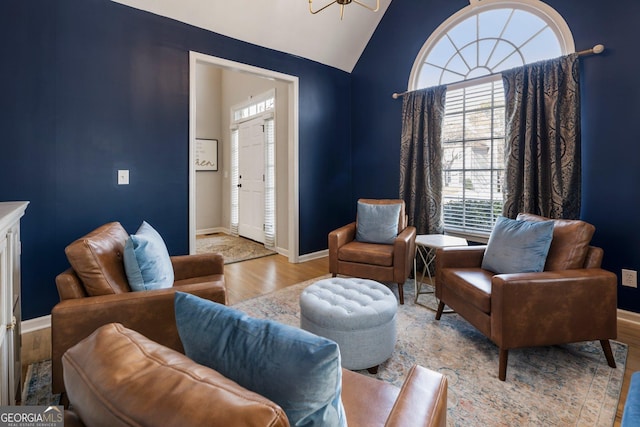 sitting room with a chandelier, light wood-type flooring, vaulted ceiling, and baseboards