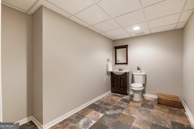 bathroom featuring baseboards, toilet, stone finish flooring, vanity, and a paneled ceiling