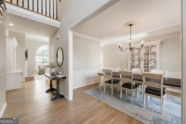 dining room with a chandelier, a wainscoted wall, visible vents, ornamental molding, and light wood finished floors