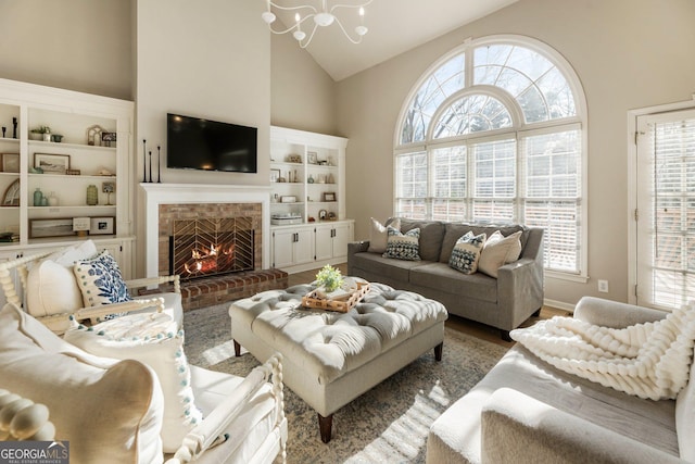 living room with high vaulted ceiling, a fireplace, wood finished floors, and an inviting chandelier