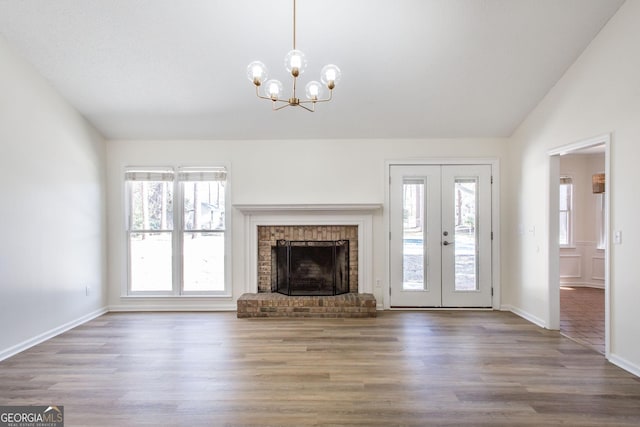 702 Hillmont Dr, Waycross, GA 31503 - unfurnished living room featuring a chandelier, wood finished floors, vaulted ceiling, french doors, and a brick fireplace