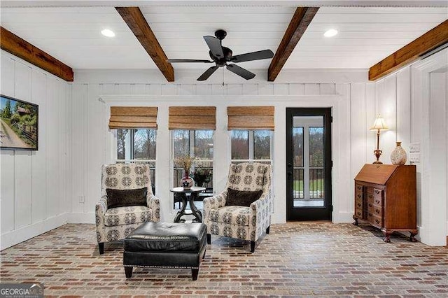 living area featuring ceiling fan, beamed ceiling, and a wealth of natural light