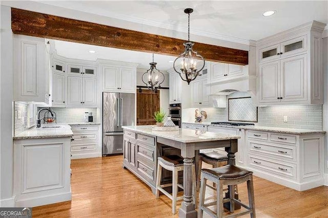 kitchen featuring appliances with stainless steel finishes, sink, a center island, white cabinetry, and decorative light fixtures