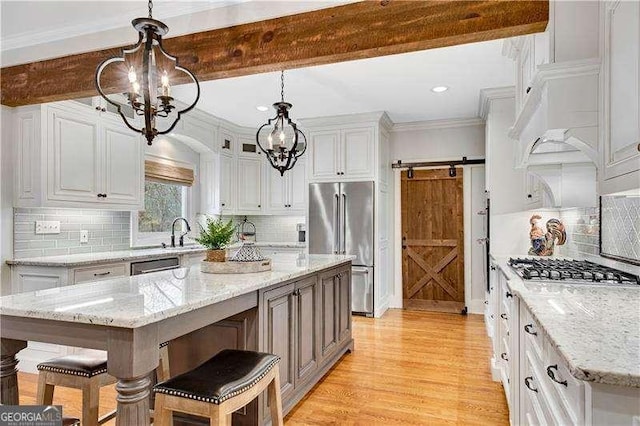 kitchen with stainless steel appliances, a center island, a barn door, light stone countertops, and pendant lighting