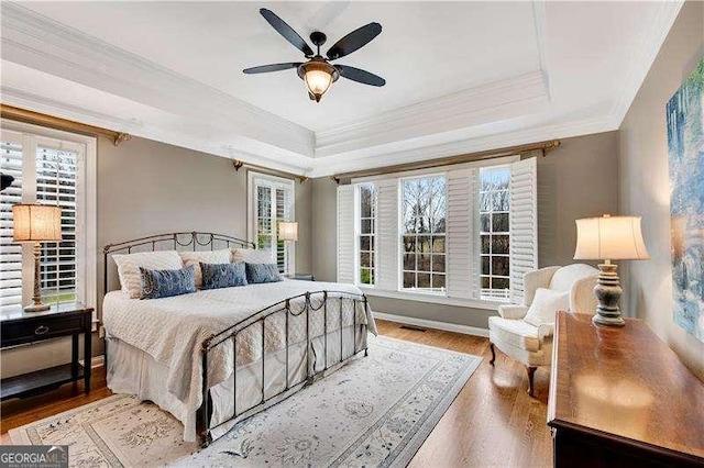 bedroom featuring wood-type flooring, ceiling fan, crown molding, and a raised ceiling