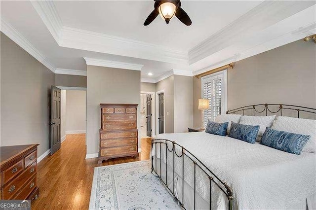 bedroom featuring a tray ceiling, ceiling fan, crown molding, and light hardwood / wood-style floors