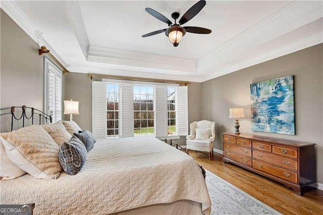 bedroom with a tray ceiling, ceiling fan, crown molding, and wood-type flooring